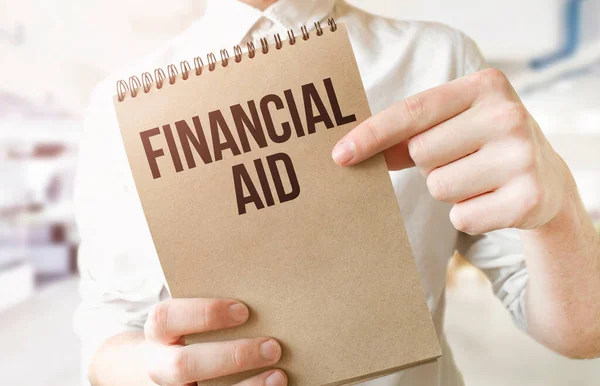 Text financial aid on brown paper notepad in businessman hands in office. Business concept