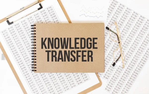 Text KNOWLEDGE TRANSFER on brown paper notepad on the table with diagram. Business concept