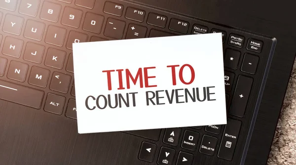 White paper sheet with text time to count revenue on the black laptop