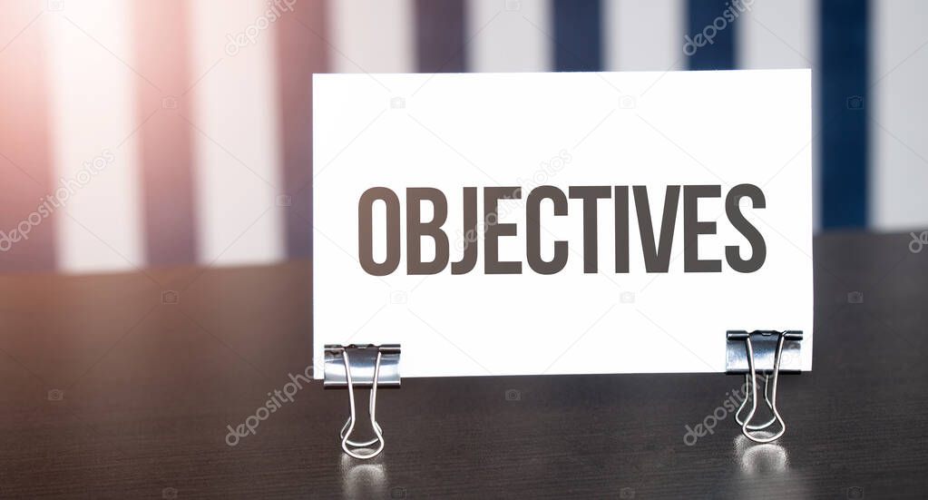 Objectives sign on paper on dark desk in sunlight. Blue and white background