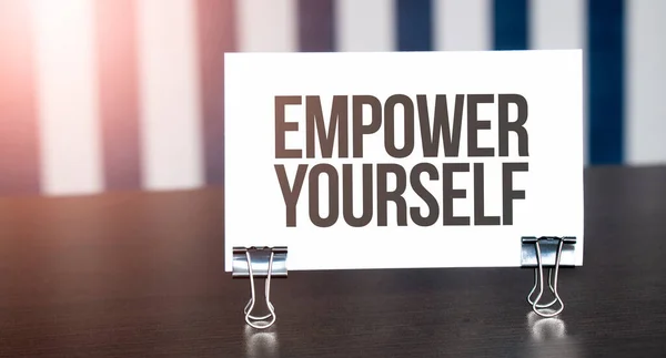 Empower Yourself sign on paper on dark desk in sunlight. Blue and white background