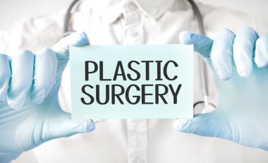 Doktor elinde kart tutuyor ve estetik ameliyat kelimesini işaret ediyor.