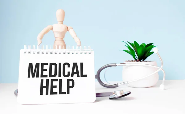 The text medical help is written on notepad and wood man toy near a stethoscope on a blue background. Medical concept