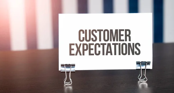 Customer Expectations sign on paper on dark desk in sunlight. Blue and white background