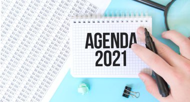 İşadamı eli, beyaz not defteri ve mali belgelerde büyüteçle birlikte. Mesaj AGENDA 2021. İş konsepti