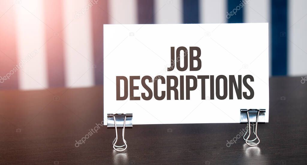 Job Descriptions sign on paper on dark desk in sunlight. Blue and white background
