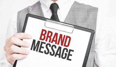 Gri arkaplanlı bir iş adamının elindeki bir defterde Brand MESSAGE yazısı var. Bir adam parmağıyla metni işaret ediyor.