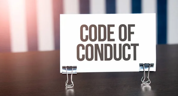 Code of Conduct sign on paper on dark desk in sunlight. Blue and white background