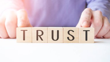 İş adamının elinde tahta küp bloğu var. Masa arkasında da güvenilir bir iş kelimesi var. Görev, Vizyon ve temel değerler kavramı