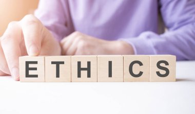 İş adamı, masa arkasında ETHICS iş sözcüğüyle tahta küp bloğu tutuyor. Görev, Vizyon ve temel değerler kavramı