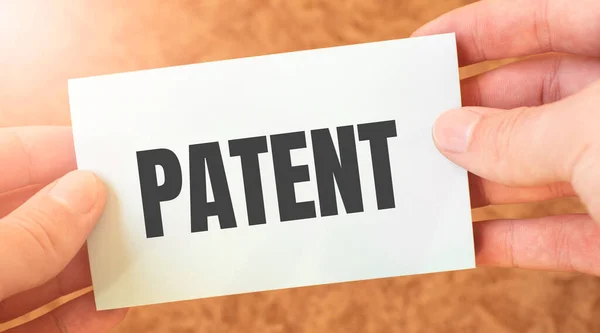 PATENT word inscription on white card paper sheet in hands of a businessman. recap concept. red and white paper