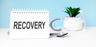 RECOVERY metni mavi arkaplanda steteskopun yanındaki not defterine yazılır. Tıbbi konsept