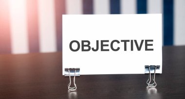 Karanlık masadaki güneş ışığı kağıdına OBJECTIVE işareti. Mavi ve beyaz arkaplan
