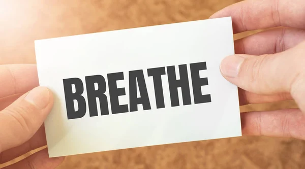 breathe word inscription on white card paper sheet in hands of a businessman. recap concept. red and white paper