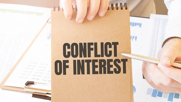 Text conflict of interest on brown paper notepad in businessman hands on the table with diagram. Business concept
