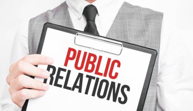 Gri arkaplanlı bir iş adamının elindeki bir defterde Halkla İlişkiler yazılıydı.