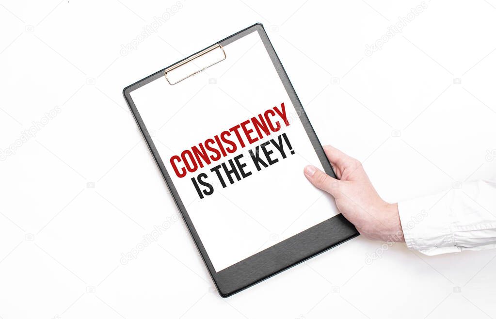 A businessman holds a folder with paper sheet with the text Consistency is the key. Business concept.