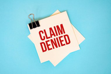 CLAIM 'e kırmızı arkaplanda izole edilmiş kopyalama alanı ve ataç içeren yapışkan notlara DENIED metni. Finans ve ekonomi konsepti.