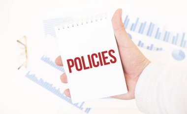 İş adamı elinde POLICIES yazılı beyaz bir not defteri tutuyor, iş konsepti