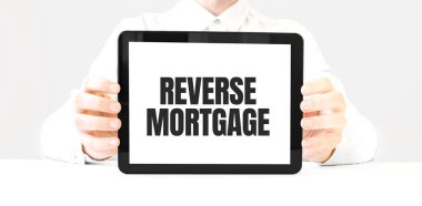 Tablet üzerindeki REVERSE MortGage metni beyaz fırında işadamlarının ellerinde. İş konsepti