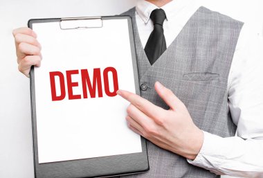 Gri arkaplanlı bir iş adamının elindeki bir defterde DEMO yazıları var. Bir adam parmağıyla metni işaret ediyor.