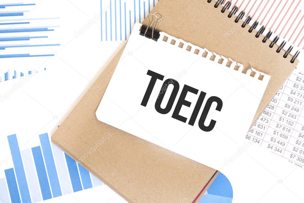Text TOEIC on white paper sheet and brown paper notepad on the table with diagram. Business concept