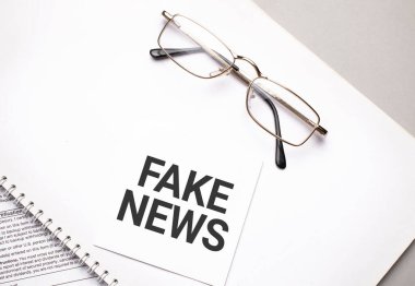 Business concept. Notebook with text FAKE NEWS sheet of white paper for notes and glasses in the grey background