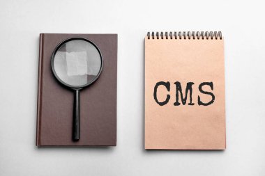 Metin CMS ile renklendirilmiş not defteri. Üzerinde büyüteç olan not defteri. İş konsepti