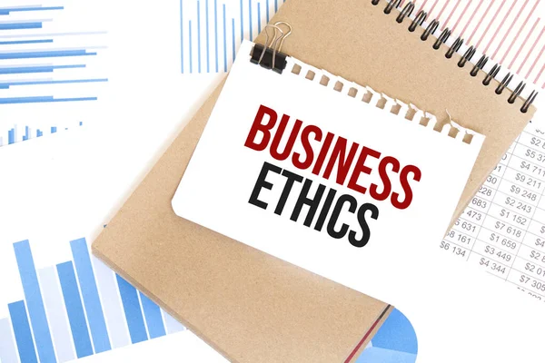 Text Business Ethics on white paper sheet and brown paper notepad on the table with diagram. Business concept