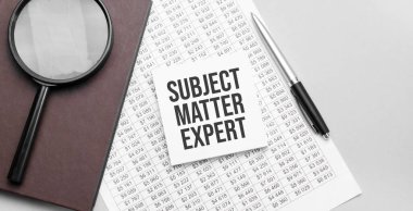 Büyüteç, finansal belge, Gri arkaplan üzerinde kahverengi defter ve SUBJECT MATTER Uzman işareti ile beyaz kağıt levha.