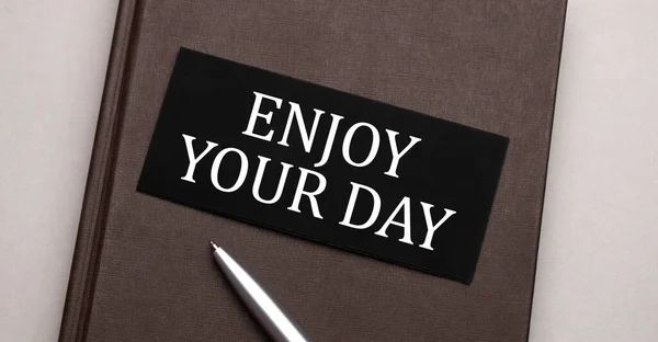 Enjoy Your Day sign written on the black sticker on the brown notepad. Tax concept