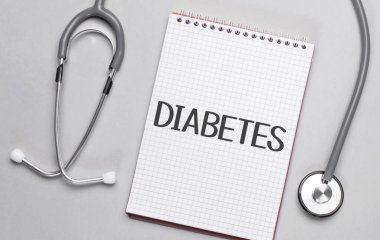 Bej bir arka plan, steteskop ve üzerinde DIABETES.Tıbbi konsept yazan beyaz bir not defteri.
