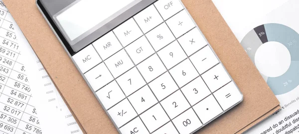 Calculator and an empty Notepad page on the office Desk with financial indicators and charts. Top view with a copy of the text input space.