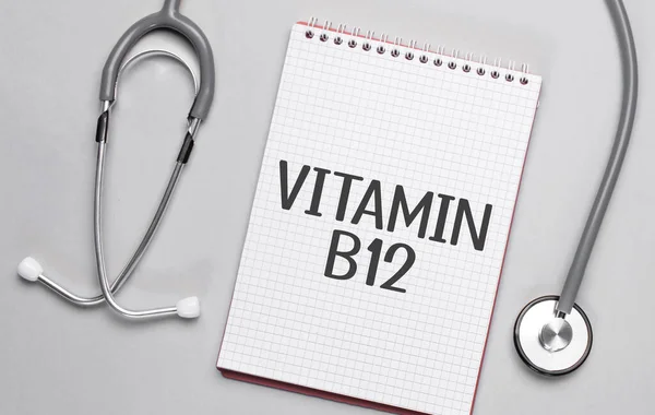 Bej bir arka plan, steteskop ve üzerinde VITAMIN B12.Medikal kavram yazan beyaz bir not defteri.