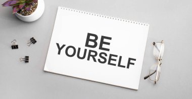 Be You SELF beyaz bir deftere siyah çerçeveli bir kalem ve yeşil bir bitkinin yanında yazılmıştır..