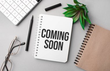Coming Soon, hesap makinesi, el işi renkli not defteri, bitki, siyah kalem ve gözlüklü beyaz bir deftere yazılmıştır..