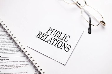 İş konsepti. Gri arkaplanda notlar ve gözlükler için beyaz kağıt halkla ilişkiler sayfası içeren not defteri