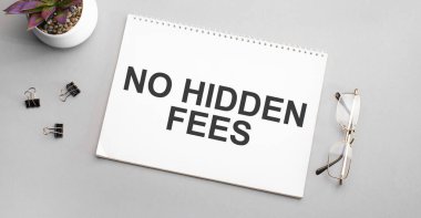 Siyah çerçeveli gözlük ve yeşil bitkinin yanındaki beyaz bir defterde gizli ücretler yazmaz..