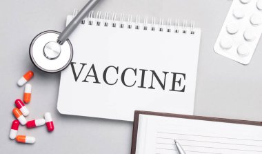 Stetoskop, haplar ve tıp masasında VACCINE metni olan defter..