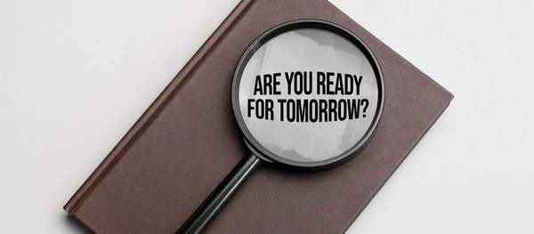 Gri arka planda kahverengi defter ve yarın tabelaya hazır mısın diye büyüteç.