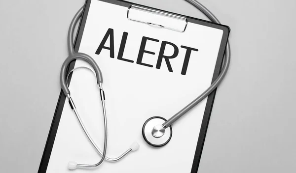 The words ALERT is written on white paper on a grey background near a stethoscope. Medical concept