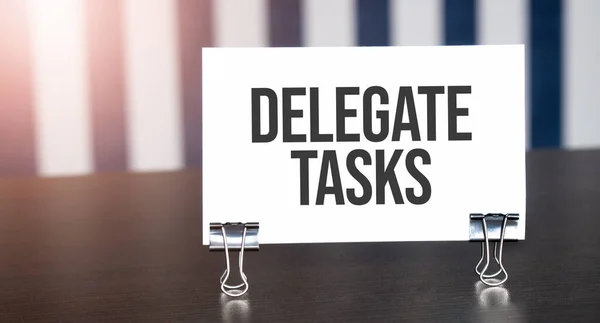 delegate tasks sign on paper on dark desk in sunlight. Blue and white background
