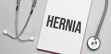 Bej bir arka plan, steteskop ve üzerinde HERNIA yazan beyaz bir not defteri. Tıbbi konsept