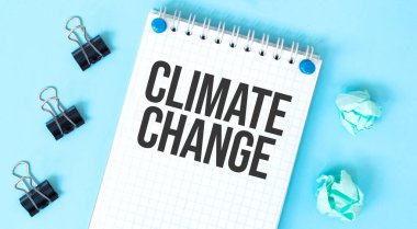 Mavi arkaplanda metin iklim değişikliği ve ofis araçlarına sahip beyaz not defteri