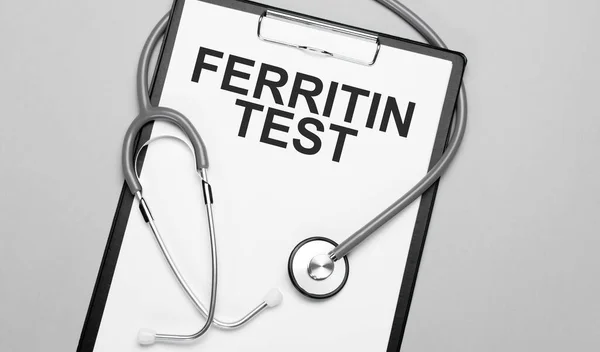 The words FERRITIN TEST is written on white paper on a grey background near a stethoscope. Medical concept