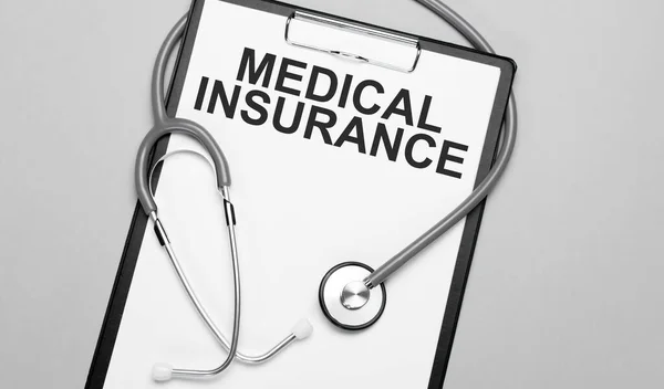 医疗保险这个词写在白纸上 背景是灰色的 靠近听诊器 医疗概念 — 图库照片