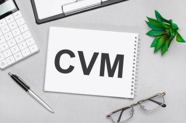 CVM gösteren metin yazılıyor. Gri arkaplanda hesap makinesi, kalem, plan, gözlük ve siyah klasör