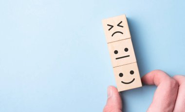 Müşteri hizmetleri değerlendirmesi ve memnuniyet araştırması konseptleri. Müşterinin eli, gülen surat ikonunu ve masadaki tahta küpten beş yıldızlı sembolü seçti.