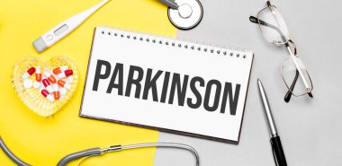 Parkinson 'a steteskop, gözlük, kalem, termometre, kırmızı haplar ve sarı arka planda kalemle mesaj at. Tıbbi konsept.