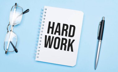 Beyaz not defteriyle zor iş kelimeleri, mavi arka planda kalem ve gözlük. Kavram